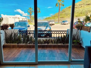 Varanda com vista para carros estacionados e palmeiras, piso de madeira e plantas em vasos.