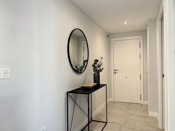 A hallway with a black-framed console table, a round mirror, and a white door at the end. - Via Celere 2328 Golf & Sea view (Casares)