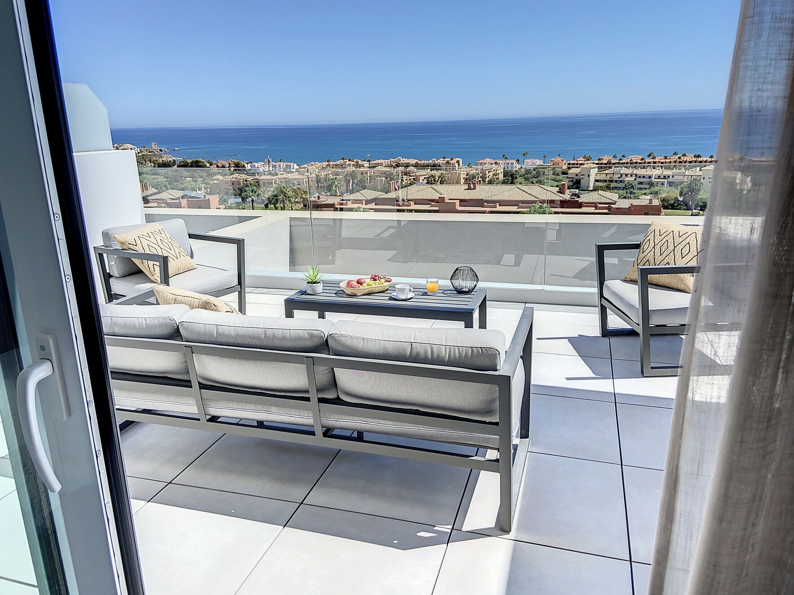A balcony with a sofa, chairs, and a table with fruit and a drink.