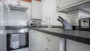 A modern kitchen with white tiled backsplash, stainless steel appliances, and a black countertop. - Honeysuckle Cottage - 1 Bedroom Cottage - Amroth (Amroth)