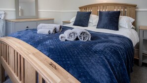 A neatly made bed with a blue blanket and rolled towels, wooden headboard, and bedside tables with lamps. - Honeysuckle Cottage - 1 Bedroom Cottage - Amroth (Amroth)