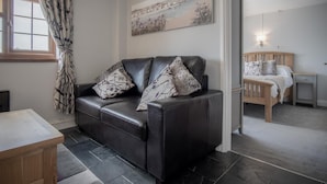 Une chambre moderne avec un canapé en cuir noir, une table de chevet en bois, un lit en bois et un tableau au mur.