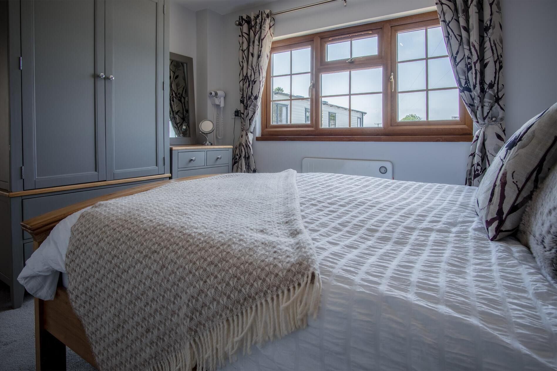 A bedroom with a bed, a wardrobe, a window with curtains, and a radiator.