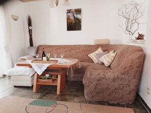 Una sala de estar acogedora con un sofá marrón, una mesa de centro de madera y una mesa de comedor preparada con copas de vino y una botella.