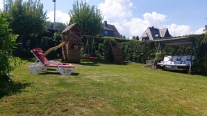 A backyard with a swing set, a slide, and a covered seating area.
