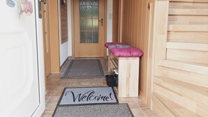A hallway with a wooden staircase, a welcome mat, and a small bench.