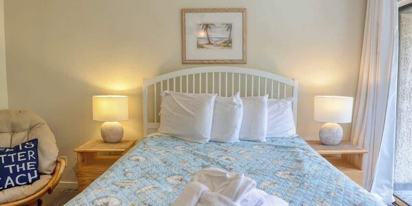 A hotel room with a bed, two bedside lamps, a chair, a framed picture on the wall, and a window with curtains.