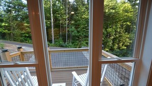 A deck with white chairs and a small table, surrounded by a wooden railing and a view of a forested area. - Dogwood Cottage (Weaverville)
