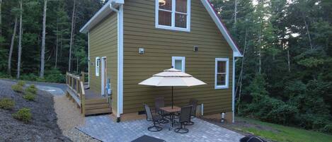 A two-story house with a patio area featuring a table and chairs, a grill, and a covered seating area.