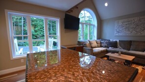 A spacious living room with a large window, a cozy sofa, and a kitchen island. - Dogwood Cottage (Weaverville)