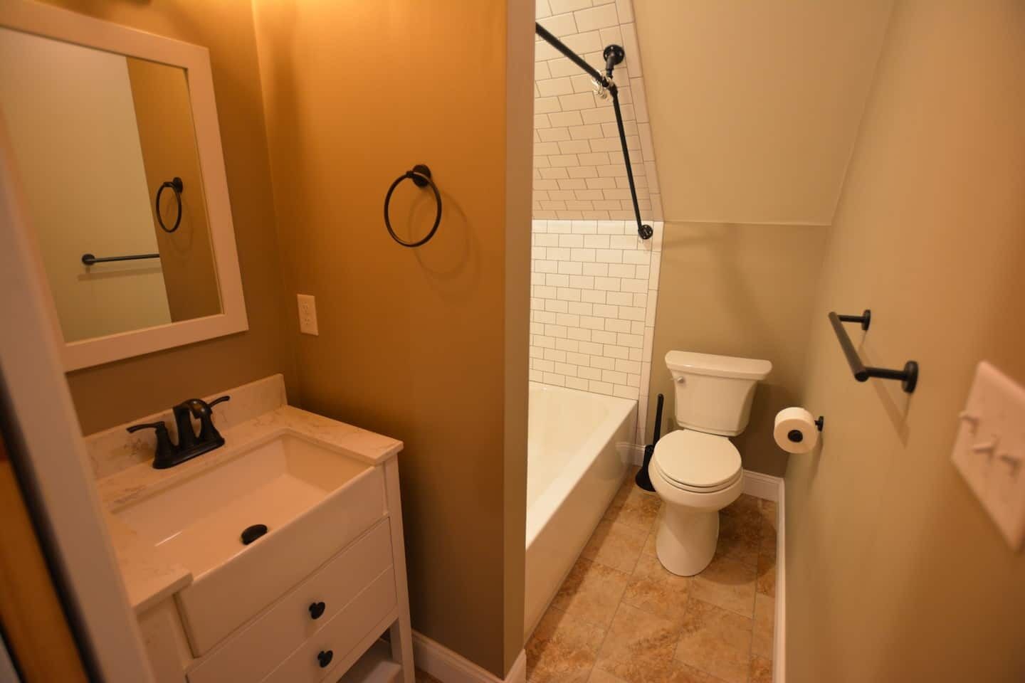 A bathroom with a white sink, mirror, toilet, and bathtub.