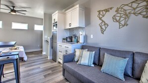 Une cuisine moderne avec des meubles blancs, un canapé gris agrémenté de coussins à motifs et un élément décoratif mural.