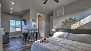 Une chambre avec un grand lit, un bureau avec deux chaises, un ventilateur de plafond et un élément décoratif mural.