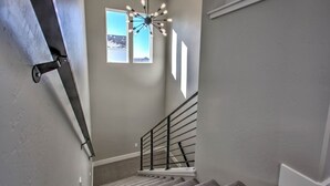 Un escalier avec une rampe en métal, des marches recouvertes de moquette et un luminaire au plafond.