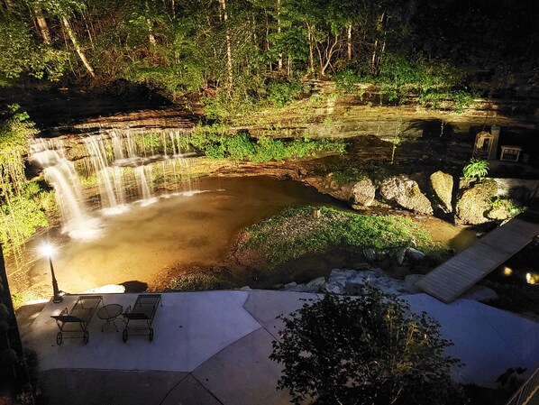A waterfall in a natural setting with a paved area and outdoor furniture. - The Loft at Old Falls (Lyles)