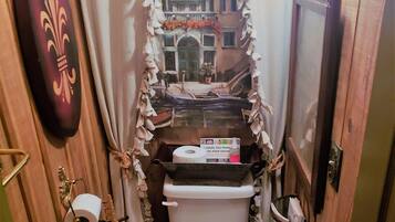 A small, narrow bathroom with a toilet, a roll of toilet paper, and a trash can.