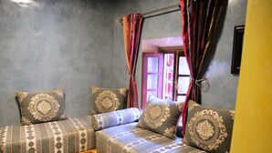 Una habitación con un sofá bajo de madera frente a una pared gris, con cojines y piso estampados.