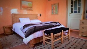 Un dormitorio con una cama de madera, un banco, un aparador y una puerta.