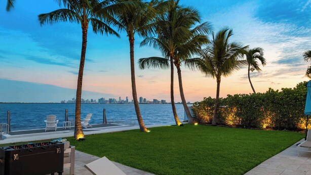 A well-maintained lawn with a foosball table, lounge chairs, and a view of the city skyline across the water. - Bayfront Villa Heated Pool Amazing Views and Beach Access (North Bay Village)
