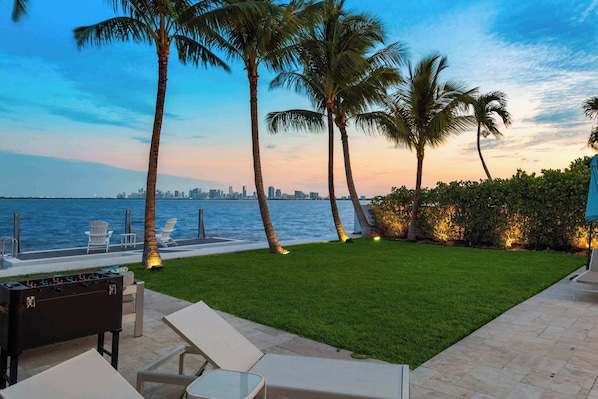 A well-maintained lawn with a foosball table, lounge chairs, and a view of the city skyline across the water.