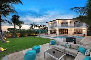 A two-story house with a swimming pool, outdoor seating, and a well-maintained lawn.
