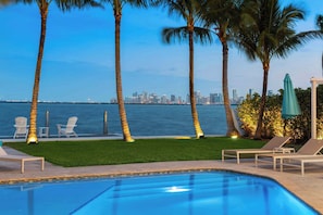 A poolside area with lounge chairs, palm trees, and a city skyline view. - Bayfront Villa Heated Pool Amazing Views and Beach Access (North Bay Village)