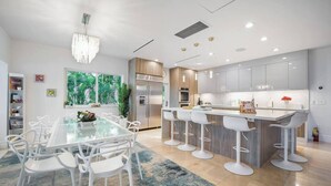 A modern kitchen with a central island, bar stools, and a dining table with chairs. - Bayfront Villa Heated Pool Amazing Views and Beach Access (North Bay Village)