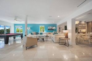 A modern living room with a pool table, a sofa set, and a dining area with chairs.