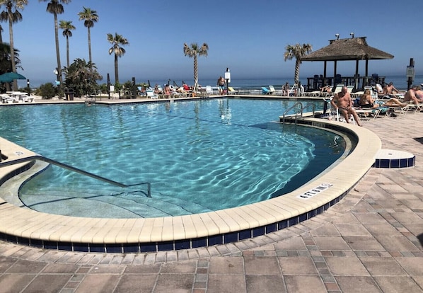 Zona de piscina con sillas de descanso y palmeras, rodeada por un deck empinado.