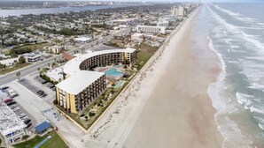 Oversigtsbillede af et kysthotel med en buet bygning, beliggende ved stranden, og udsigt til havet.