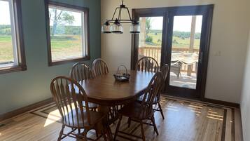 Une salle à manger avec une table et des chaises en bois, de grandes fenêtres et une vue sur l’extérieur.