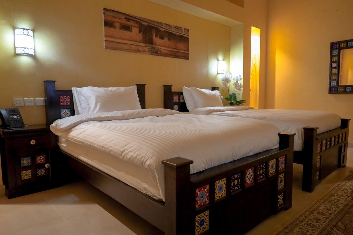 A hotel room with two beds, a nightstand with a phone, and decorative wall sconces.