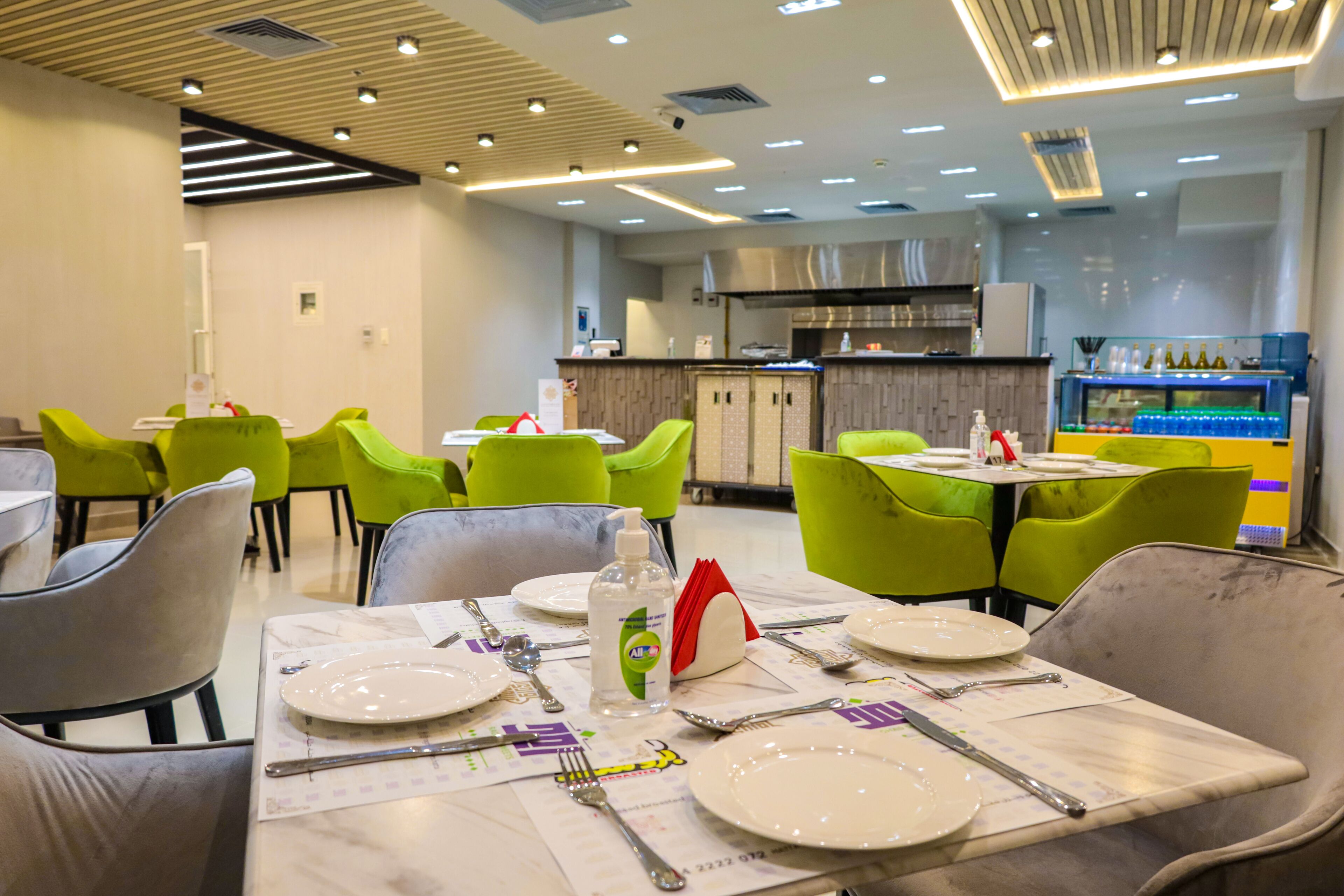 A restaurant with green chairs, white tables, and a bar area with bottles.