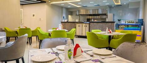 A restaurant with green chairs, white tables, and a bar area with bottles.