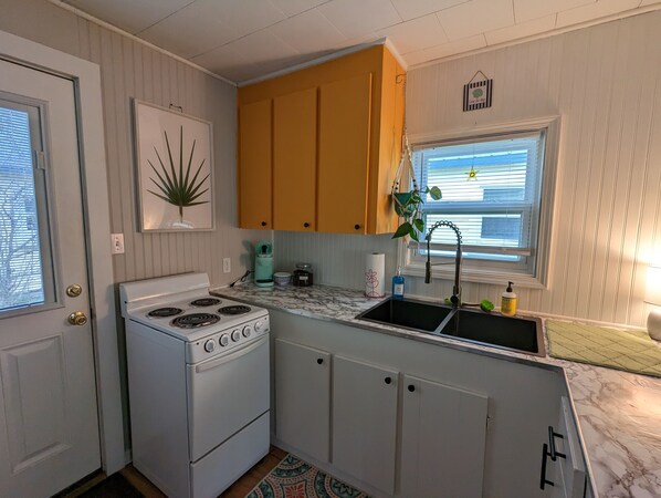 Compact kitchen with a stove, sink, and window above the sink, offering a view.