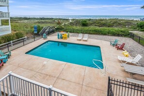 A swimming pool with lounge chairs and a view of the beach.