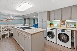 A modern kitchen with a built-in washer and dryer, wooden chairs, and a chandelier.