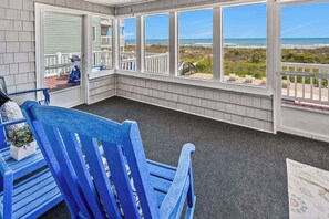 A covered outdoor area with a view of the beach, a blue chair, and a small table with a plant. - Space for the whole family! 9-bedroom oceanfront home w/fantastic pool & deck in North Myrtle (North Myrtle Beach)