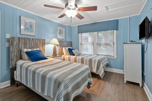 A bedroom with two beds, a ceiling fan, a lamp, and a television.