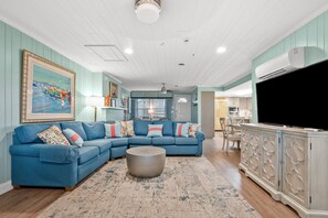 A living room with a sectional sofa, a round coffee table, and a television on a cabinet. - Space for the whole family! 9-bedroom oceanfront home w/fantastic pool & deck in North Myrtle (North Myrtle Beach)