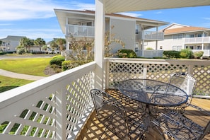 A covered patio with a round metal table and chairs, surrounded by white lattice railings.