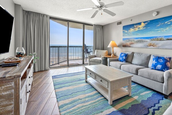 Relax in this stylish living room with a sofa set, coffee table, and TV on a stand, leading to a balcony with a beach view.
