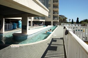 Relax by the pool with lounge chairs and umbrellas, surrounded by a white fence and hotel balconies.