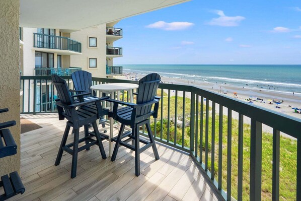 A balcony with a view of the beach, featuring a table and chairs.