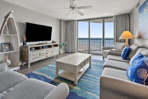 Relax in this stylish living room with a large flat-screen TV, sliding glass door to a balcony with ocean views, and a comfortable sofa.