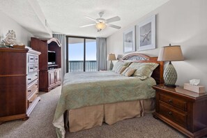 A hotel room with a bed, a dresser, a lamp, and a ceiling fan. - Light & breezy oceanfront condo rental with lazy river, pool, and fitness center near Ocean Drive (North Myrtle Beach)