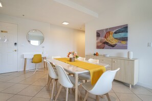 A modern dining area with a white table, yellow table runner, and white chairs.