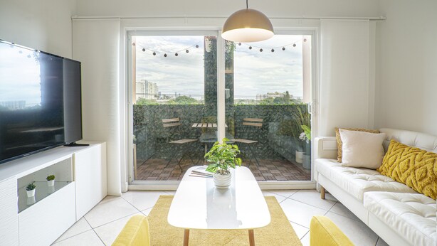 Una sala moderna con un televisor de pantalla plana, una mesa de comedor, un sofá y un amplio ventanal corredero que da a un patio exterior.