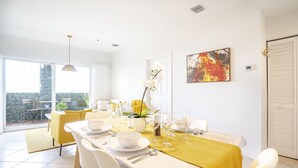 Un comedor luminoso con una mesa dispuesta para seis comensales, un mantel amarillo y un amplio ventanal con vistas a un jardín.