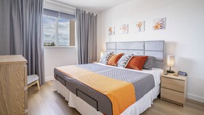 Un dormitorio con cama, mesita de noche, lámpara y una obra de arte en la pared.
